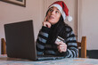 © AliciaFdez - Una mujer joven con un sombrero rojo de santa sentada frente a la computadora portátil y sosteniendo una tarjeta de crédito. Concepto de compra online
