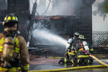 A Residential Home Burns In A House Fire As Firefighters Spay Water From A Hose In An Effort To Put It Out. 
