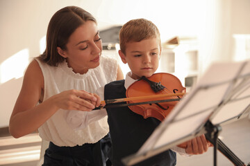 Canvas Print - Young woman teaching little boy to play violin indoors