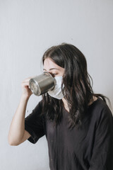 Armenian girl tries to drink tea from an iron mug, but does it with difficulty due to the mask mode