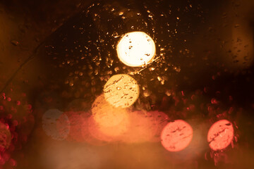 Wall Mural - Abstract bokeh blur background by rain drops on glass window at night in the city