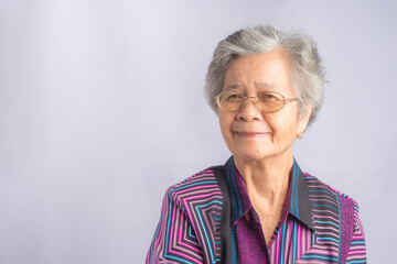 Portrait of a beautiful senior Asian woman wearing glasses with short white hair smiling and looking at the camera while standing with a gray background. Concept of aged people and healthcare