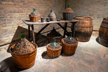 Ancient Wine Barrels And Demijohns In A Cellar.