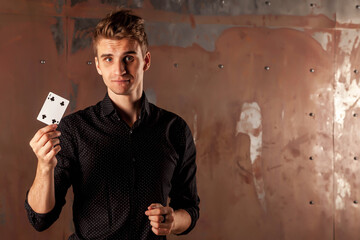 Close-up portrait of young man with gambling cards. Handsome guy shows tricks with card. Clever hands of magician on metal texture background. Concept of entertainment and Hobbies. Copy space