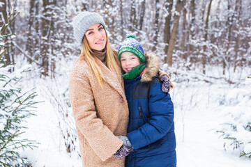 Portrait of happy mother with child son in winter outdoors. Snowy park. Single parent.