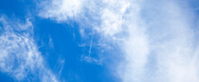 Airplane In The Blue Sky With Clouds From Below, High Flying Passenger Plane With Condensation Trail. Jet Plane Flying Overhead Diagonally In Sky With Sunlight. Bottom View