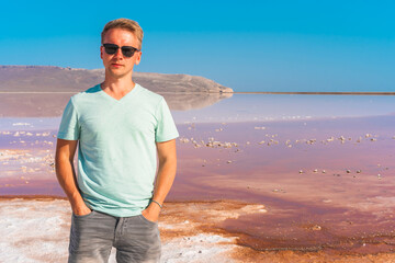 Canvas Print - A happy young man in sunglasses stands near a pink salt lake in Crimea