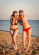© kravik93 - Mom and teenage daughter, looking at the camera and blowing you a kiss, have a slim body, wear bikini sunglasses, posing in front of a tropical beach. The concept of family happiness