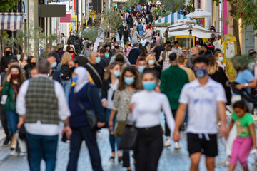 crowd goes up and down a busy shopping street wearing a protective mask