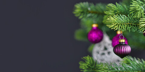 Wall Mural - Banner with beautiful purple glass tree bauble on decorated Christmas tree with other seasonal tree ornaments on dark black background with empty copy space