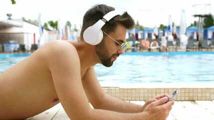 Poster - Handsome young man with mobile phone listening to music near swimming pool at resort