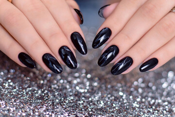 Beautiful female hands with fashion manicure nails, black gel polish, on glitter background