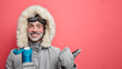 Cheerful bearded male skier with happy expression enjoys winter recreation dressed in warm jacket gloves covered with snow drinks hot beverage from thermos goes in for extreme sport in mountains