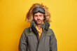 © WHstudio Leushin N - Photo of displeased man has active winter rest looks with annoyed expression at camera raises eyebrows dressed in warm thermal jacket with hood isolated over yellow background. Seasonal recreation
