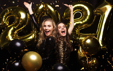 Happy gorgeous girls in stylish sexy party dresses holding gold 2021 balloons, having fun at New Year's Eve Party.