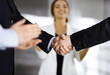 © cameravit - Businessmen are shaking hands while standing with colleagues applauding in office, close-up. Business success concept
