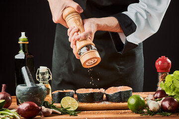 Chef using a pepper mill over raw salmon steaks