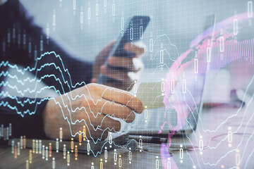 Double exposure of man's hands holding and using a phone and financial graph drawing. Analysis concept.