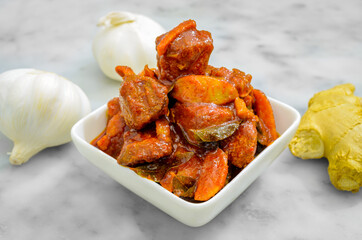 Closeup of fried fish pickle in a bowl along with whole garlic & ginger