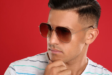 Wall Mural - Handsome man wearing sunglasses on red background, closeup