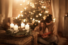 Child Sits With Mother In Front Of The Christmas Tree And Read A Book Together And Look Forward To Christmas, Advent Wreath