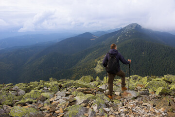 Adventurous man is standing with a backpack on top of the mountain. Tourism, travel, climbing, hiking, active leisure concept