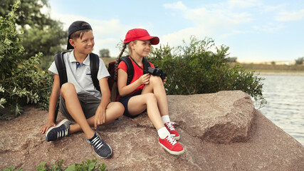 Sticker - Cute little children with backpacks sitting on rock near river. Camping trip