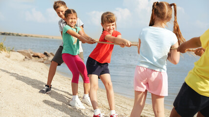 Sticker - Cute little children playing tug of war game near river on sunny day