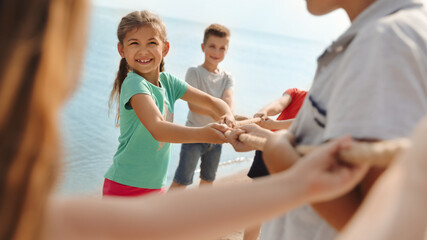 Wall Mural - cute little children playing tug of war game near river on sunny day
