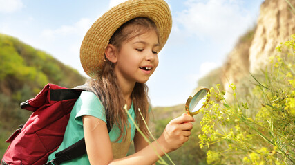 Poster - Cute little girl exploring plant with magnifying glass outdoors on sunny day