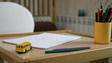 Close-up Toy Yellow School Bus Paper And Pencils On Empty Desk In Room. Education At Home. Blurred Background Pictures Bed. 2x Slow Motion 60 Fps 4K