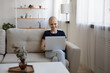 © fizkes - Smiling hairless woman using laptop, sitting on cozy couch in living room, happy young female enjoying leisure time with gadget, having fun online, chatting or shopping, watching video or movie