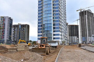 Wall Mural - Wheel loader on road building at construction site. Earth-moving heavy equipment for road work. Tower cranes construct of modern residential buildings. Construction machinery and civil engineering