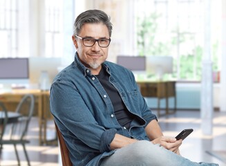 older man sitting at home in living room using mobile phone.