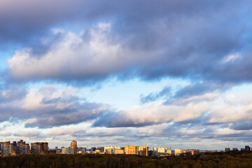 Wall Mural - low gray clouds in blue sky over city lit by sunset sun in autumn twilight