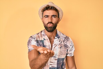 Wall Mural - Young hispanic man wearing summer hat looking at the camera blowing a kiss with hand on air being lovely and sexy. love expression.