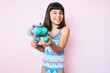Young little girl with bang wearing swimsuit and watergun winking looking at the camera with sexy expression, cheerful and happy face.