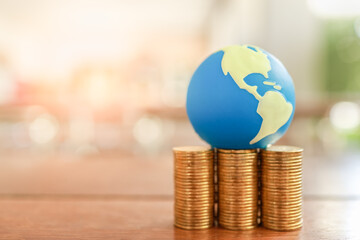 Global Business and Financial, Economic and palnning Concept. Close up of mini world ball on stack of gold coins on wooden table with copy space.