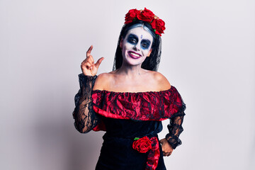 Sticker - Young woman wearing mexican day of the dead makeup smiling and confident gesturing with hand doing small size sign with fingers looking and the camera. measure concept.