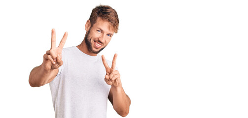 Young caucasian man wearing casual white tshirt smiling looking to the camera showing fingers doing victory sign. number two.