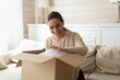 © fizkes - Preparing to relocation. Happy smiling young female buyer tenant renter of new flat packing with love and care at moving day, pleased excited millennial lady receiving unboxing expected postal parcel