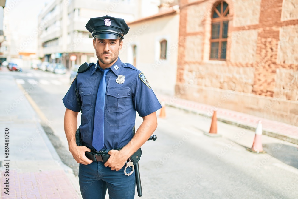 young handsome hispanic policeman wearing police uniform. Standing with serious expression at town street.