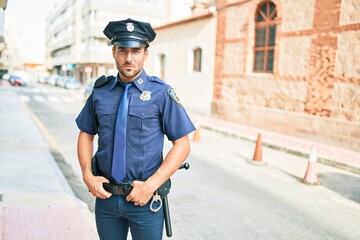 Poster - young handsome hispanic policeman wearing police uniform. Standing with serious expression at town street.