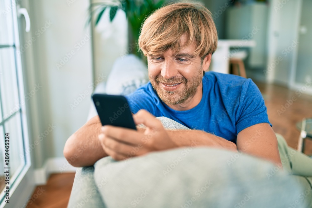 Middle age handsome caucasian man relaxing at sitting on the sofa at home with smartphone - obrazy, fototapety, plakaty 