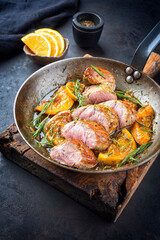 Wall Mural - Traditional fried pork filet medaillons in with orange slices and herbs offered as close-up in a rustic wrought iron skillet