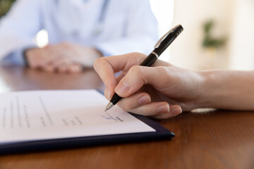 Successful negotiations. Close up of young female hand holding pen able to put her name on paper contract, insurance policy, signing sale or purchase agreement in presence of agent manager consultant