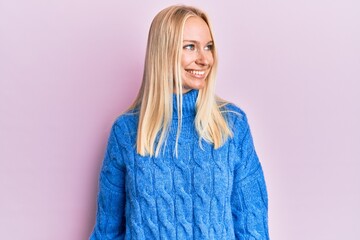 Wall Mural - Young blonde girl wearing wool winter sweater looking away to side with smile on face, natural expression. laughing confident.