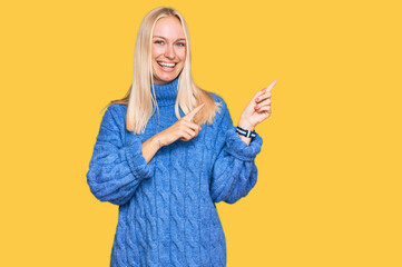 Wall Mural - Young blonde girl wearing wool winter sweater smiling and looking at the camera pointing with two hands and fingers to the side.