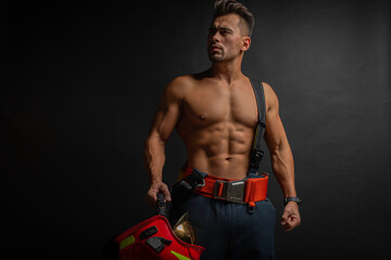 Wall Mural - portrait of a muscular, handsome firefighter on a dark background, holding a fire helmet, looking to the side