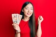 Young chinese woman holding 10 united kingdom pounds banknotes screaming proud, celebrating victory and success very excited with raised arm